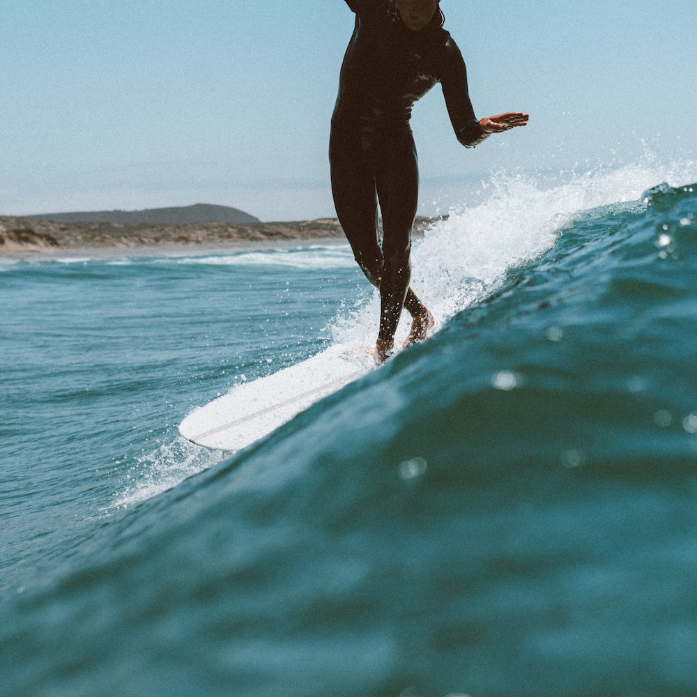 Person surfing on a wave in the ocean with clear blue sky.
