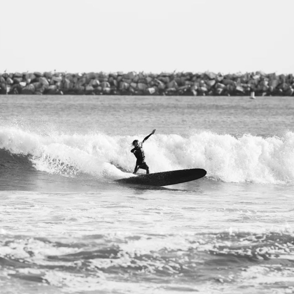 Person surfing on a wave with a rocky shoreline in the background