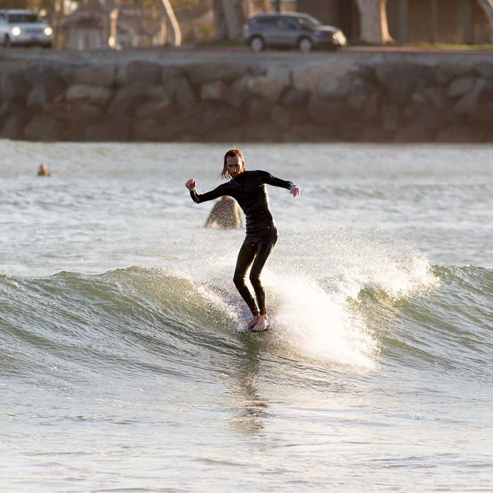 Person surfing on a wave in a wetsuit with a cityscape in the background