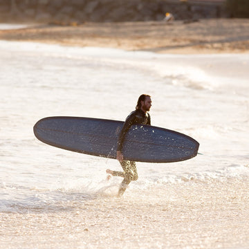 Person holding a surfboard on a beach with waves in the background