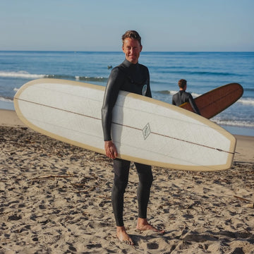 Person holding a surfboard on a beach with another person in the background