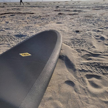Surfboard on a sandy beach with a person in the distance