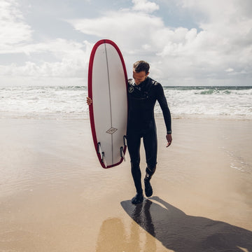 Man in a wetsuit holding a surfboard on a beach with ocean waves in the background