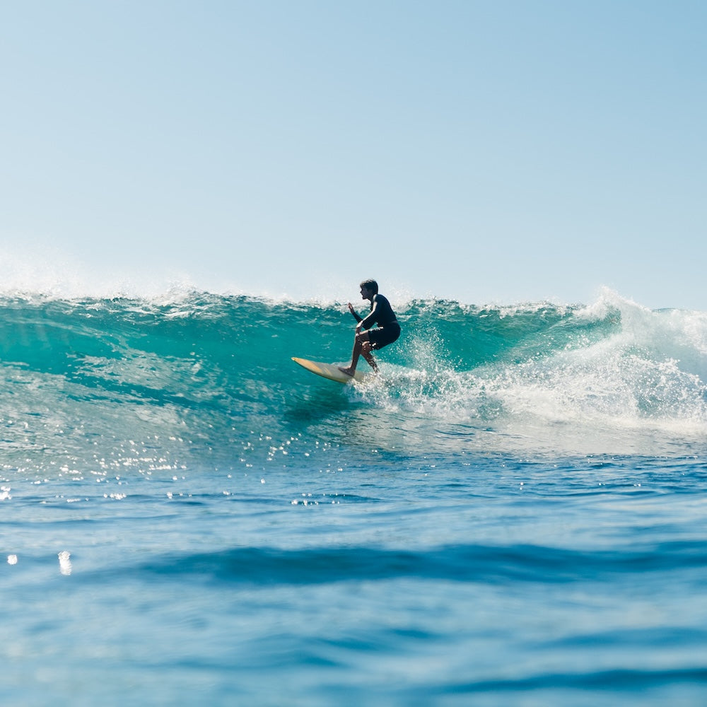 Person surfing on a wave in clear blue water with a clear sky.