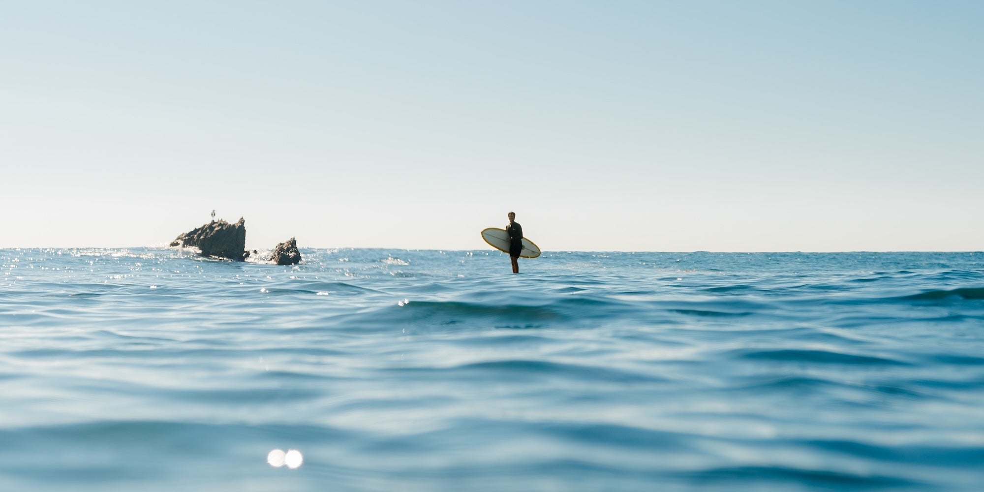 Person on a surfboard in the ocean with a clear sky
