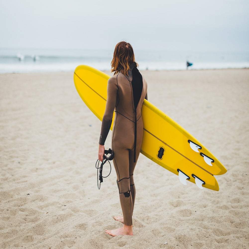 Person in a wetsuit holding a yellow surfboard on a beach