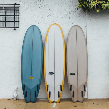 Three surfboards of different colors leaning against a white wall.