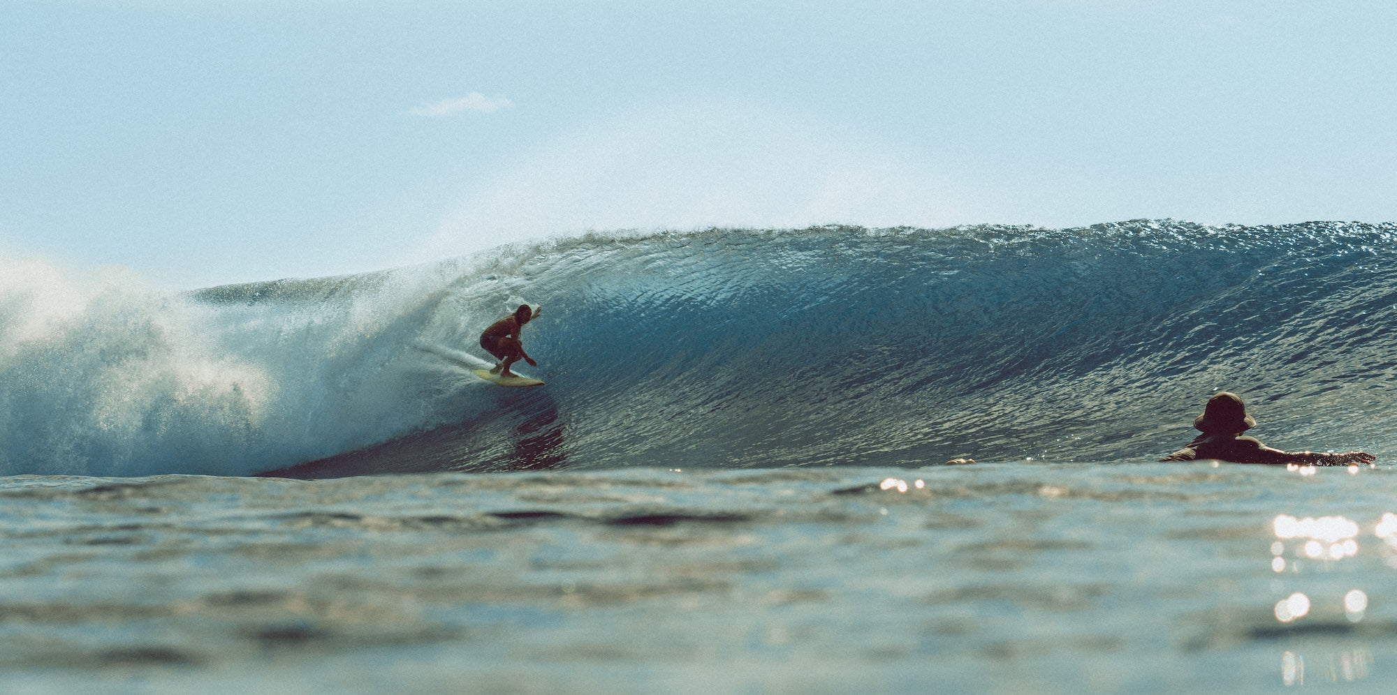 Surfer riding a wave with another person watching in the water.