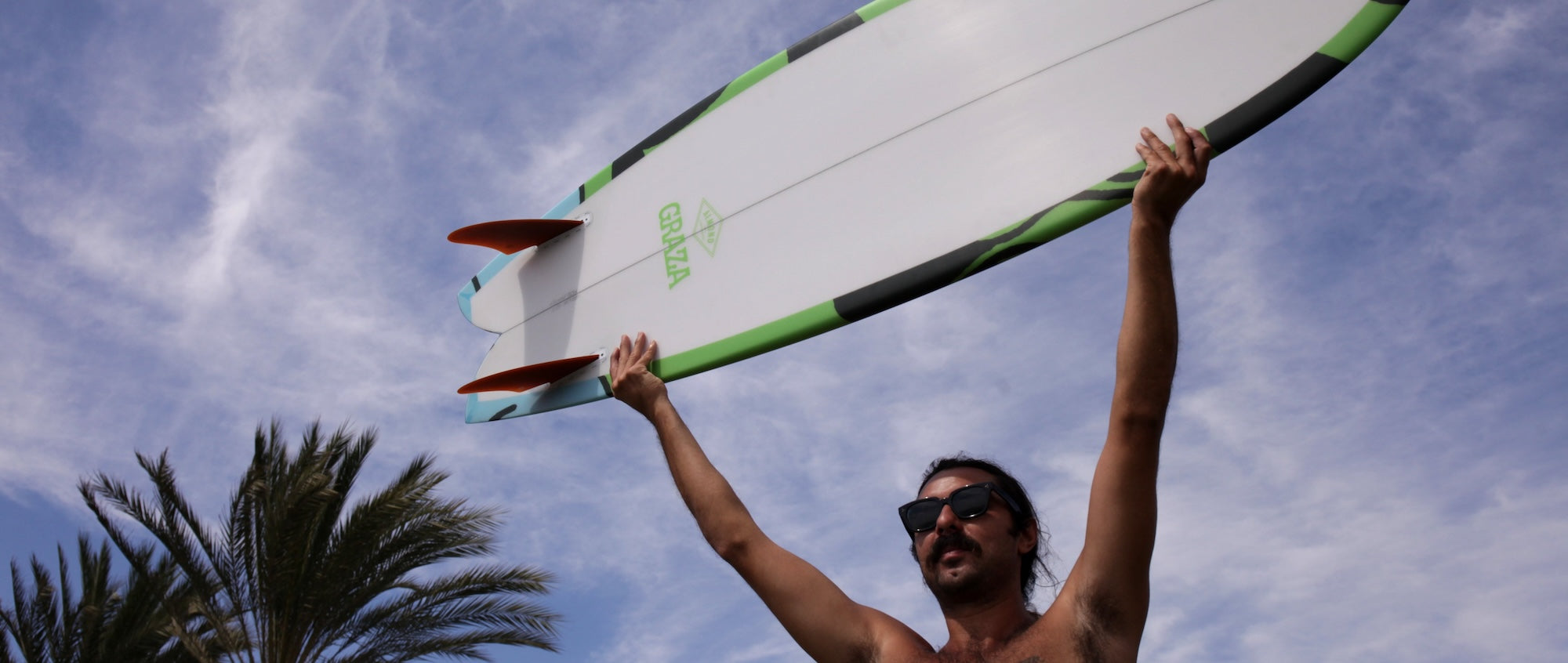Man holding a surfboard against a blue sky with cloudsslider_item_qNYVqF