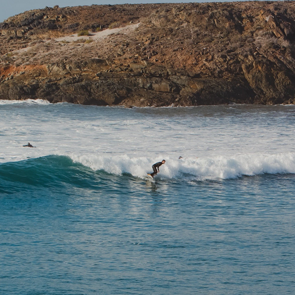 Person surfing a wave with rocky cliffs in the background