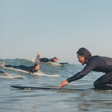 Surfers in wetsuits paddling on surfboards in the ocean with a clear sky.