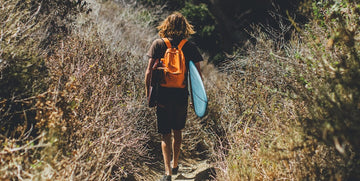Person hiking through a forest carrying a backpack and surfboard
