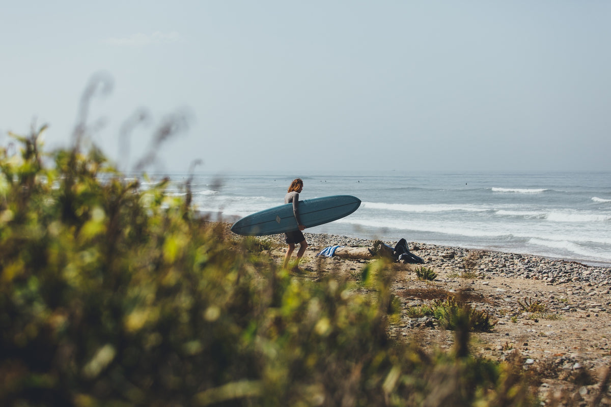 Person holding a surfboard walking along a beach with waves and sky in the background