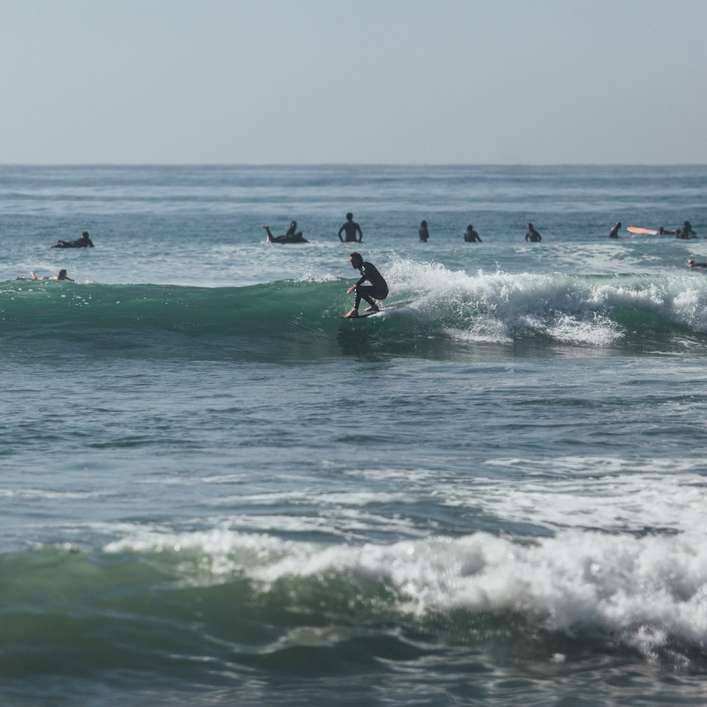 Surfer riding a wave with other surfers in the background on a sunny day.