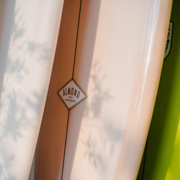 Close-up of a surfboard with 'Almond' branding against a blurred natural background