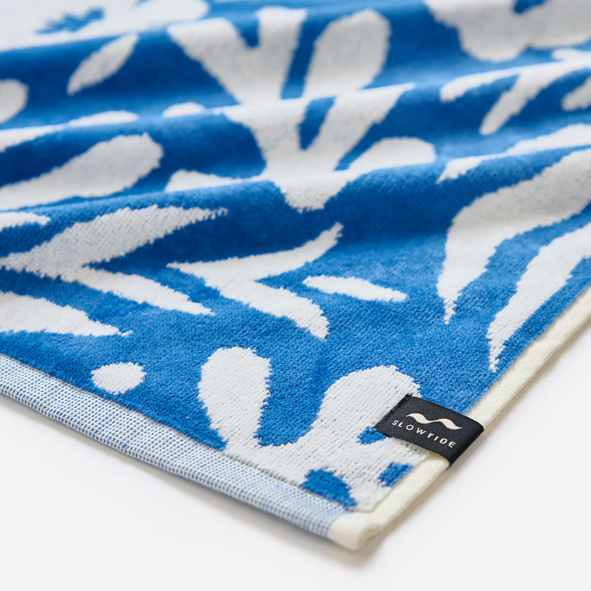 Blue and white patterned towel with a Slowtide label on a white background