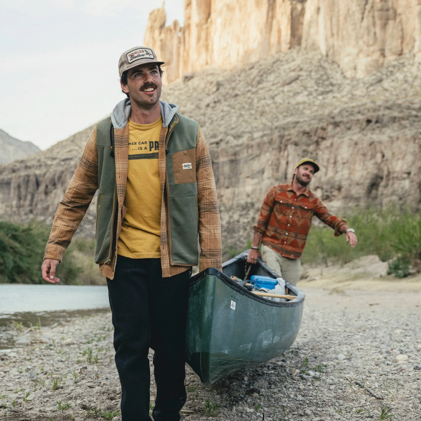 Two men carrying a canoe with a canyon in the background