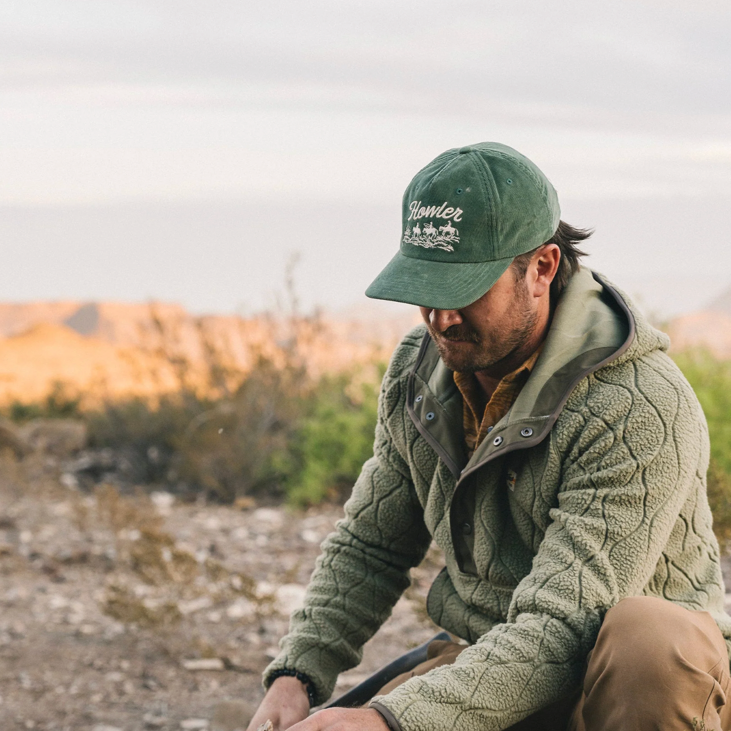 Man wearing a green cap and jacket outdoors with a blurred natural background