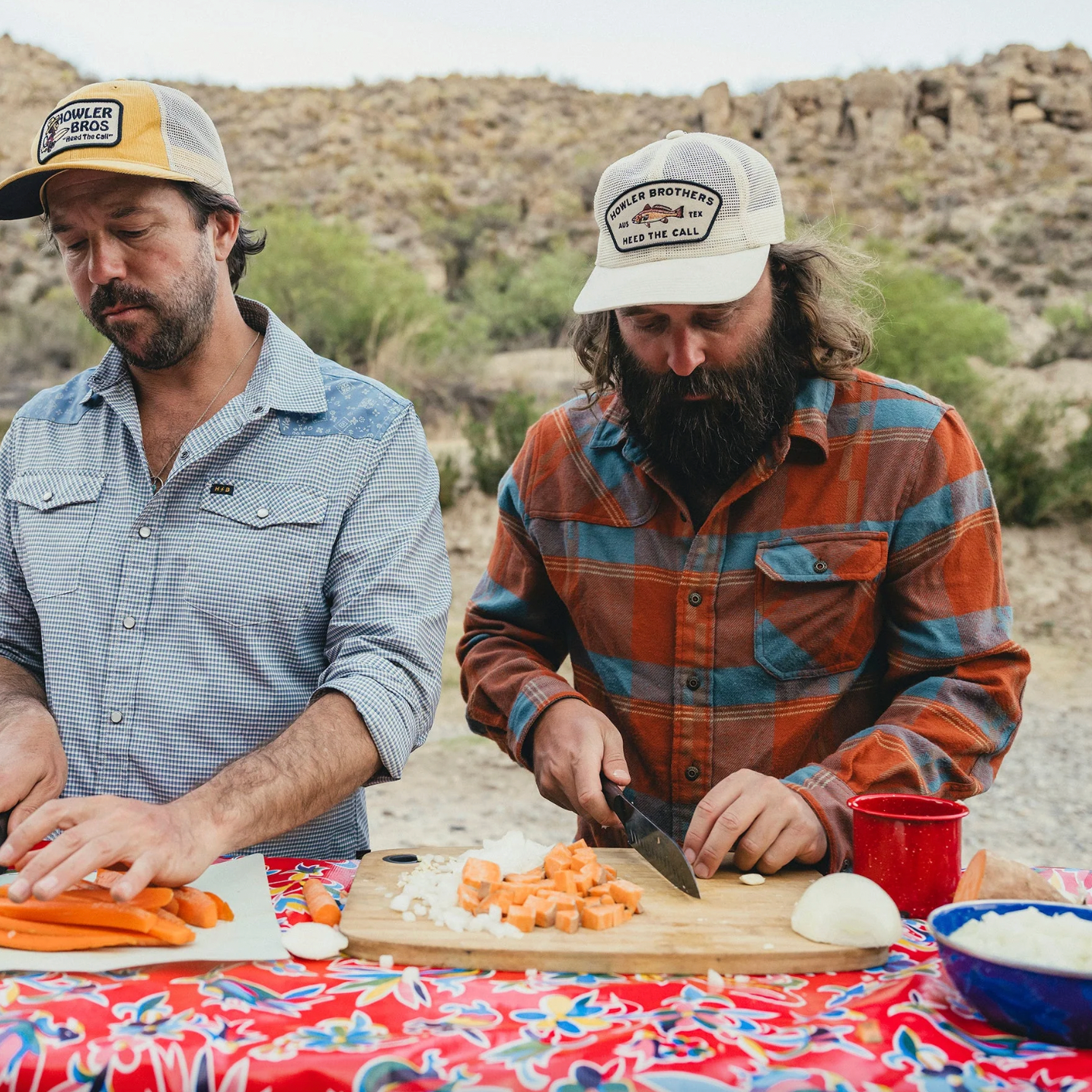 Two men preparing food outdoors with a desert landscape in the background