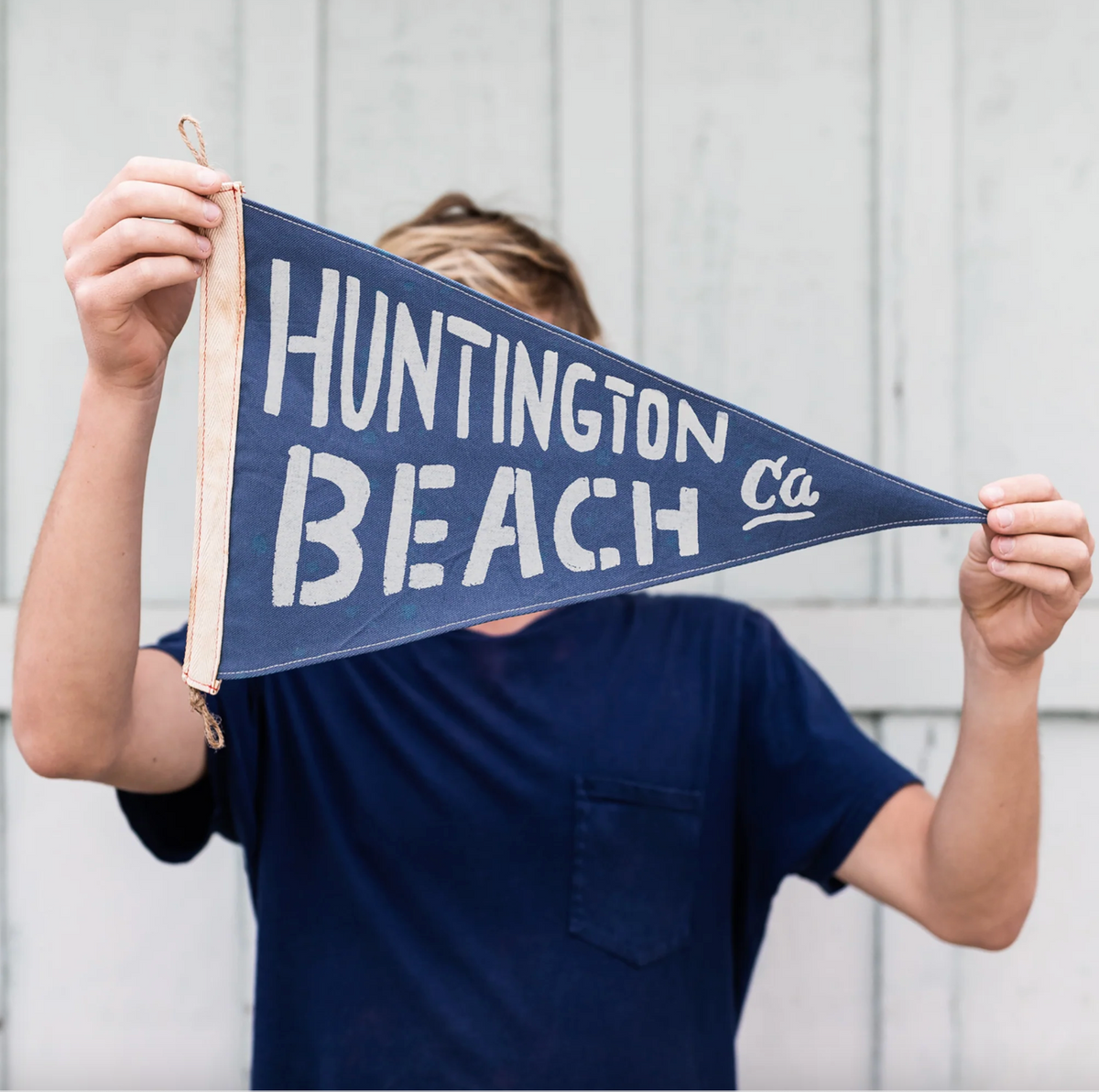 Person holding a blue and white 'Huntington Beach, Ca' pennant against a light background