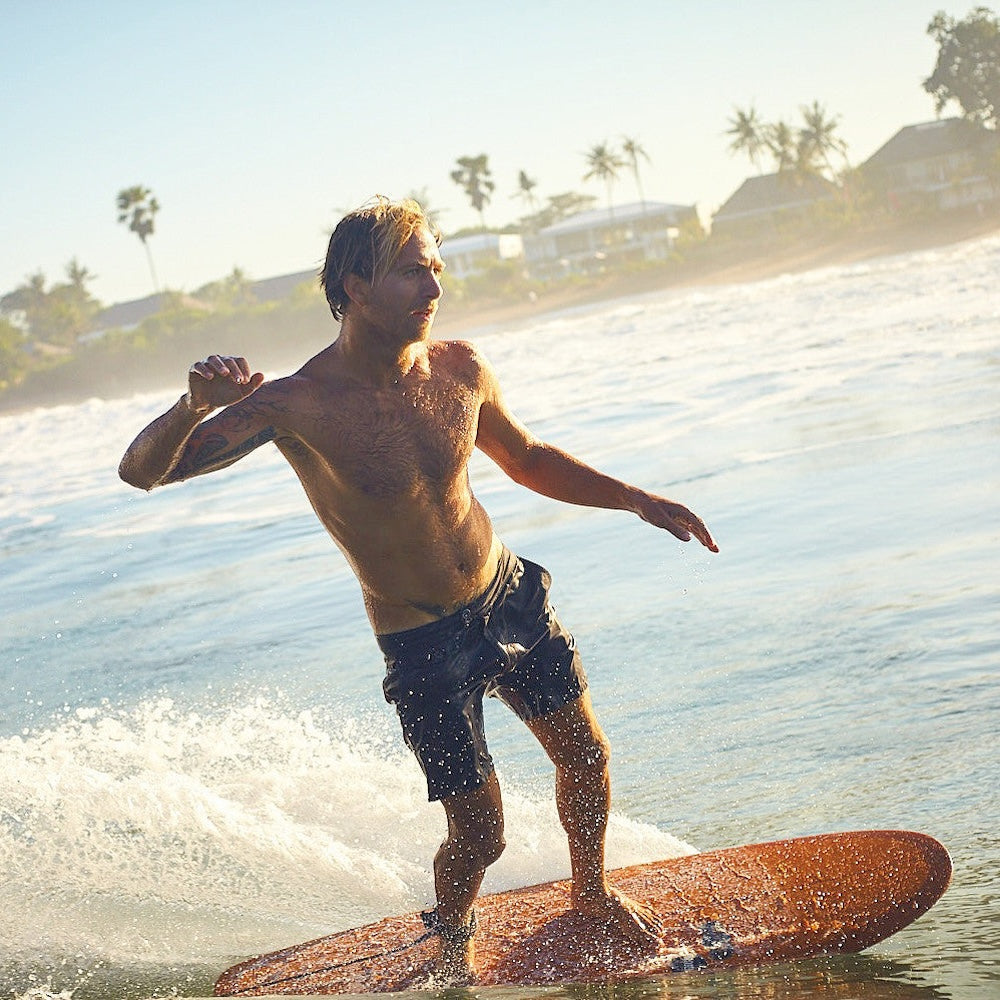 Man surfing on a wave with palm trees and buildings in the background