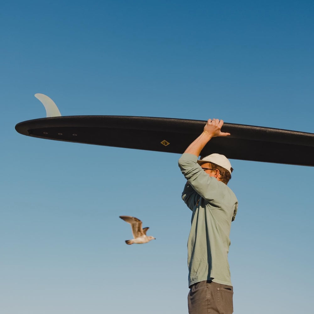 man holding a black surfboard against clear blue sky