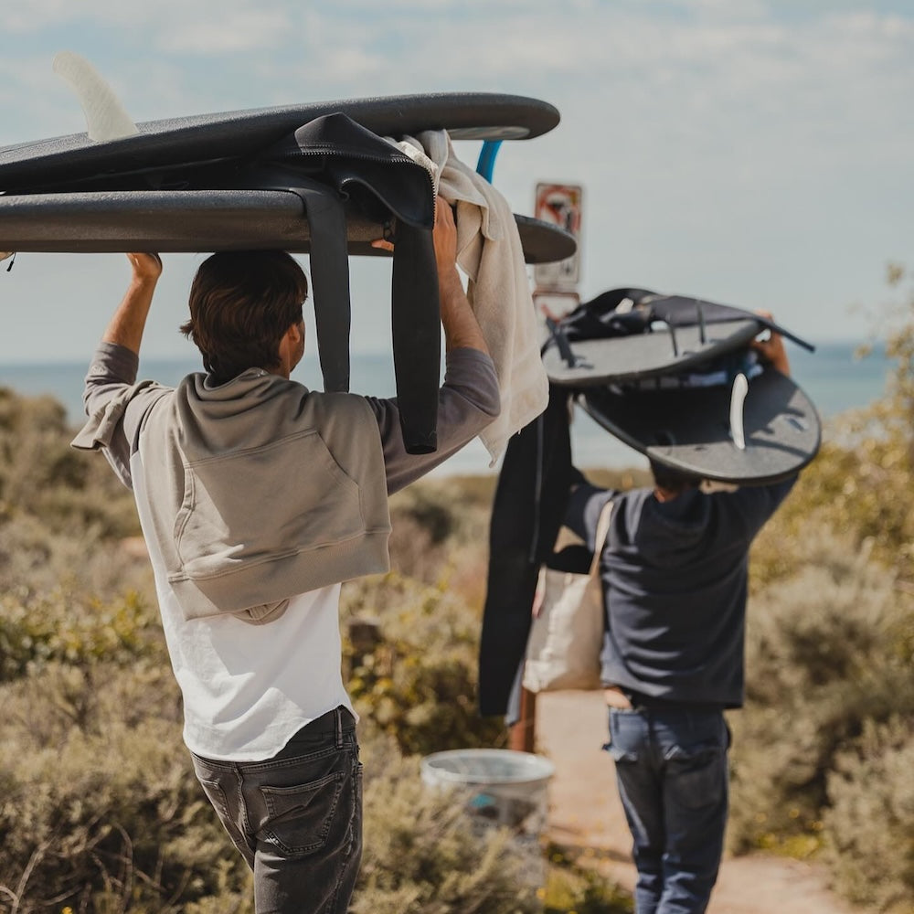 Two people carrying surfboards over their heads on a trail with a scenic background.
