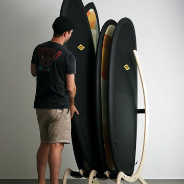 Person standing next to a rack of surfboards against a plain wall