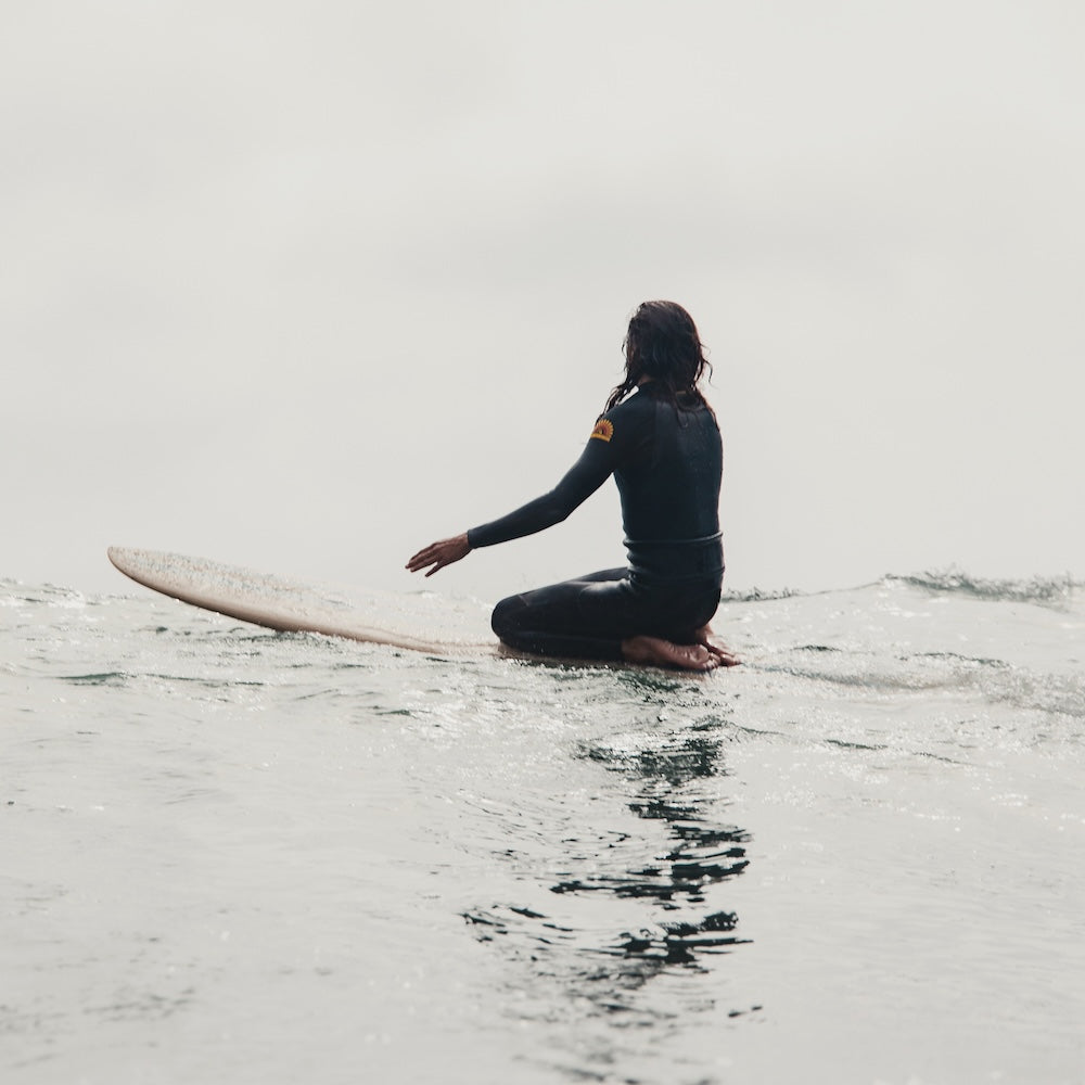Person in a wetsuit sitting on a surfboard in calm water