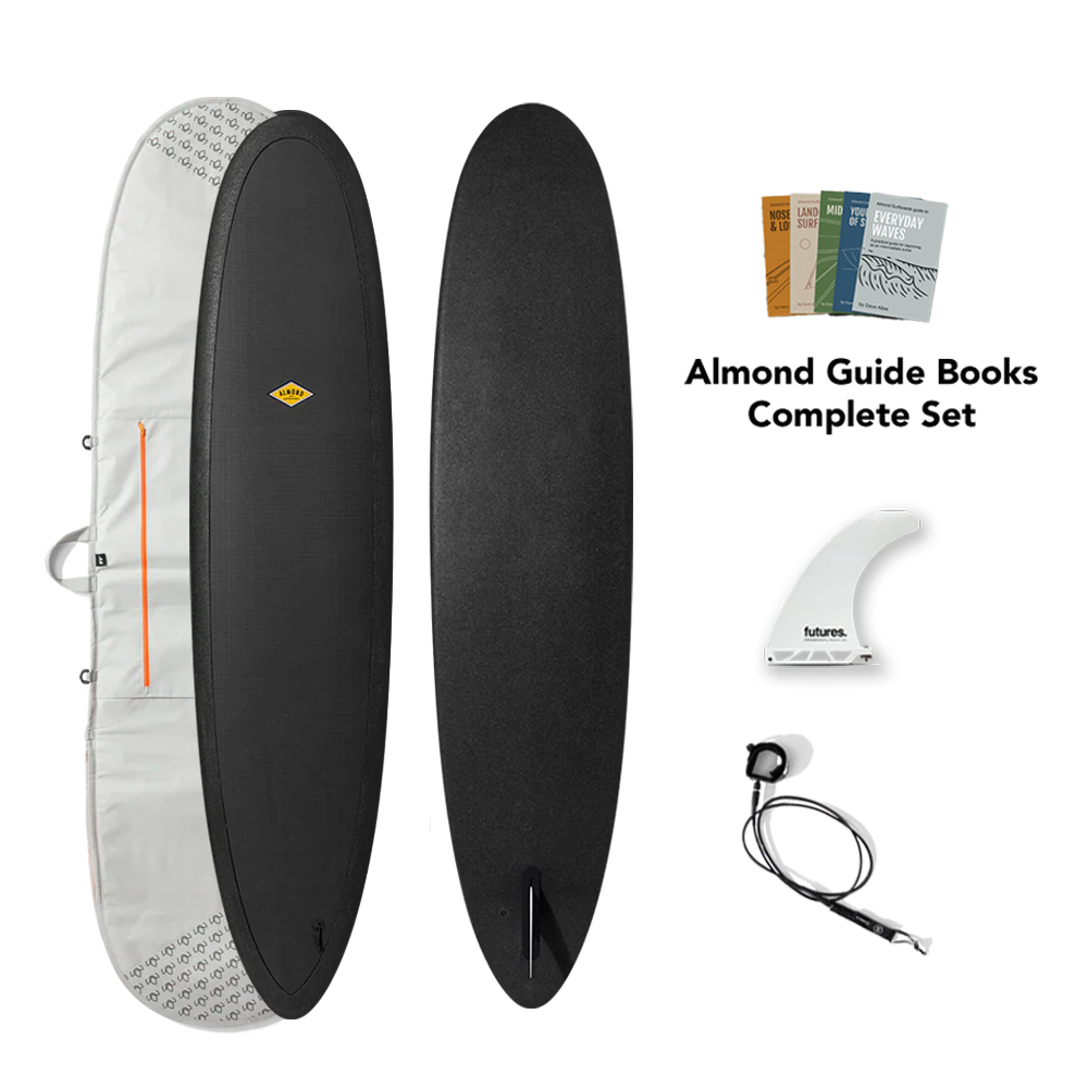 Black surfboard with accessories including a cover, fins, and guide books on a white background