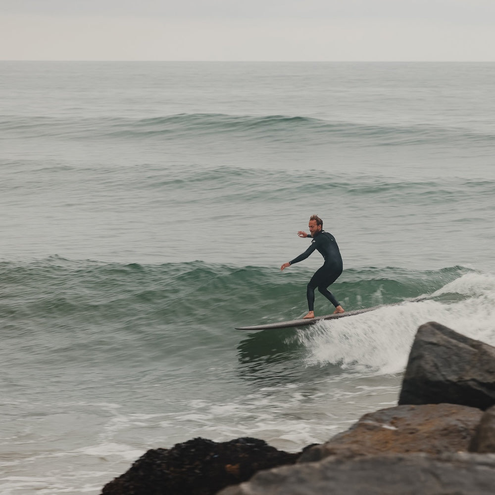 Person surfing on a wave near rocks with a cloudy sky
