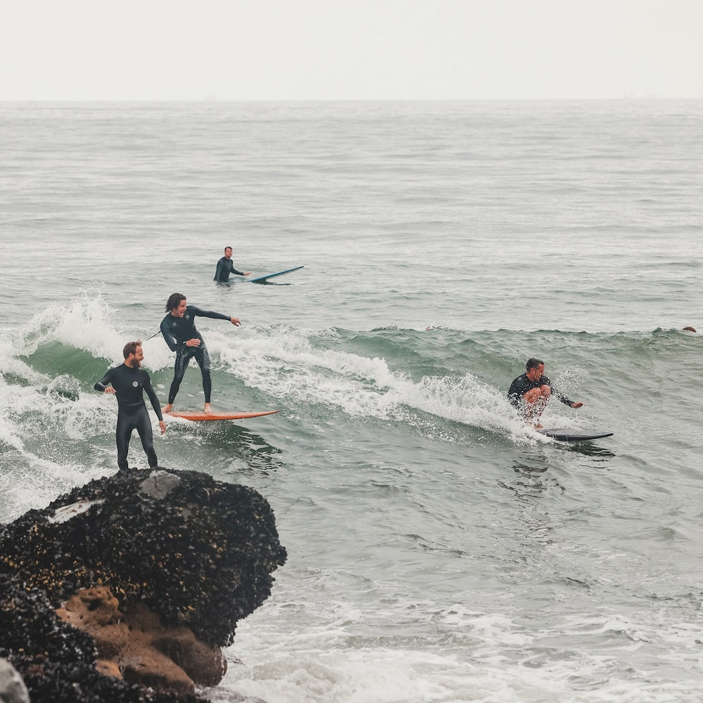 Four people surfing a wave near a rocky coastline