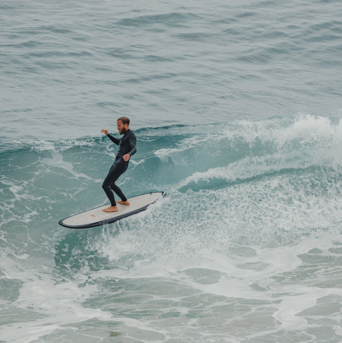 Black surfboard with accessories including a cover, fins, and guide books on a white background