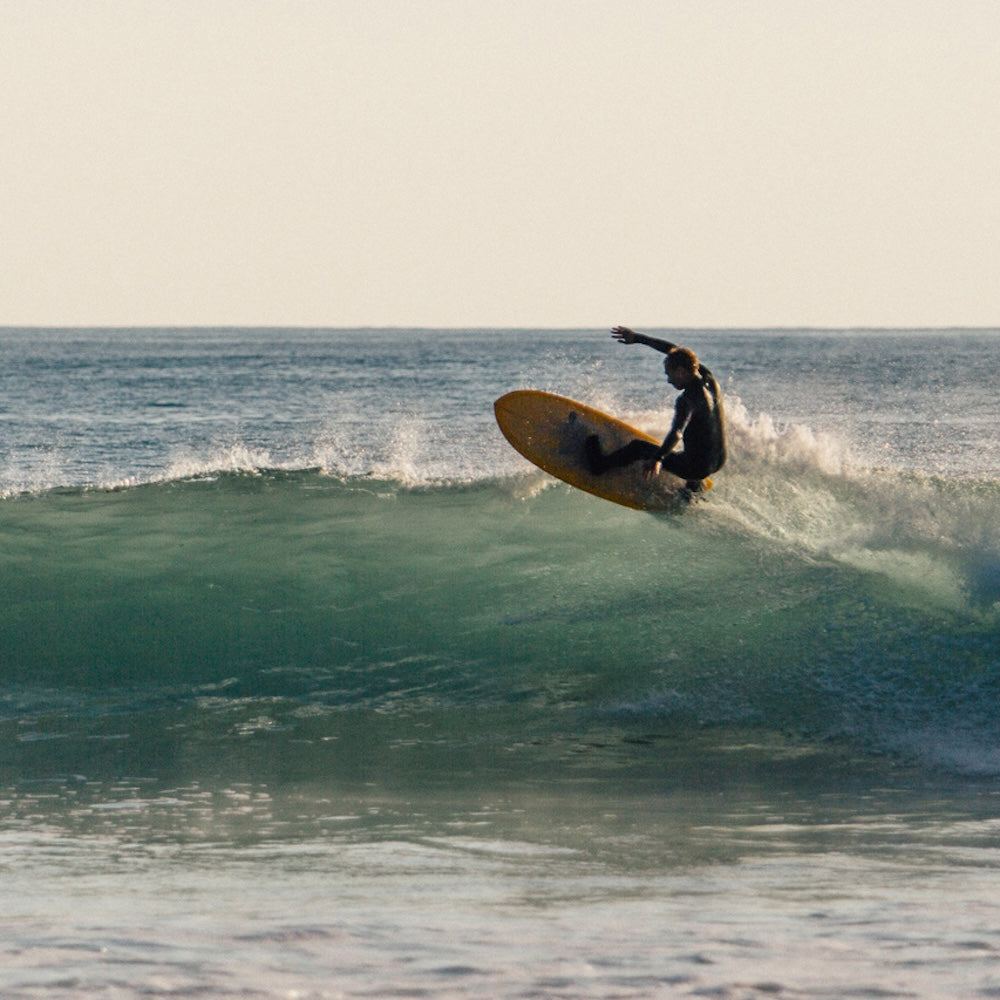 Person surfing on a wave in the ocean with a clear sky.