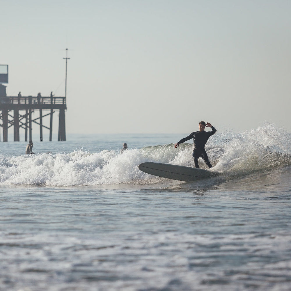 Person surfing on a wave with a pier in the background