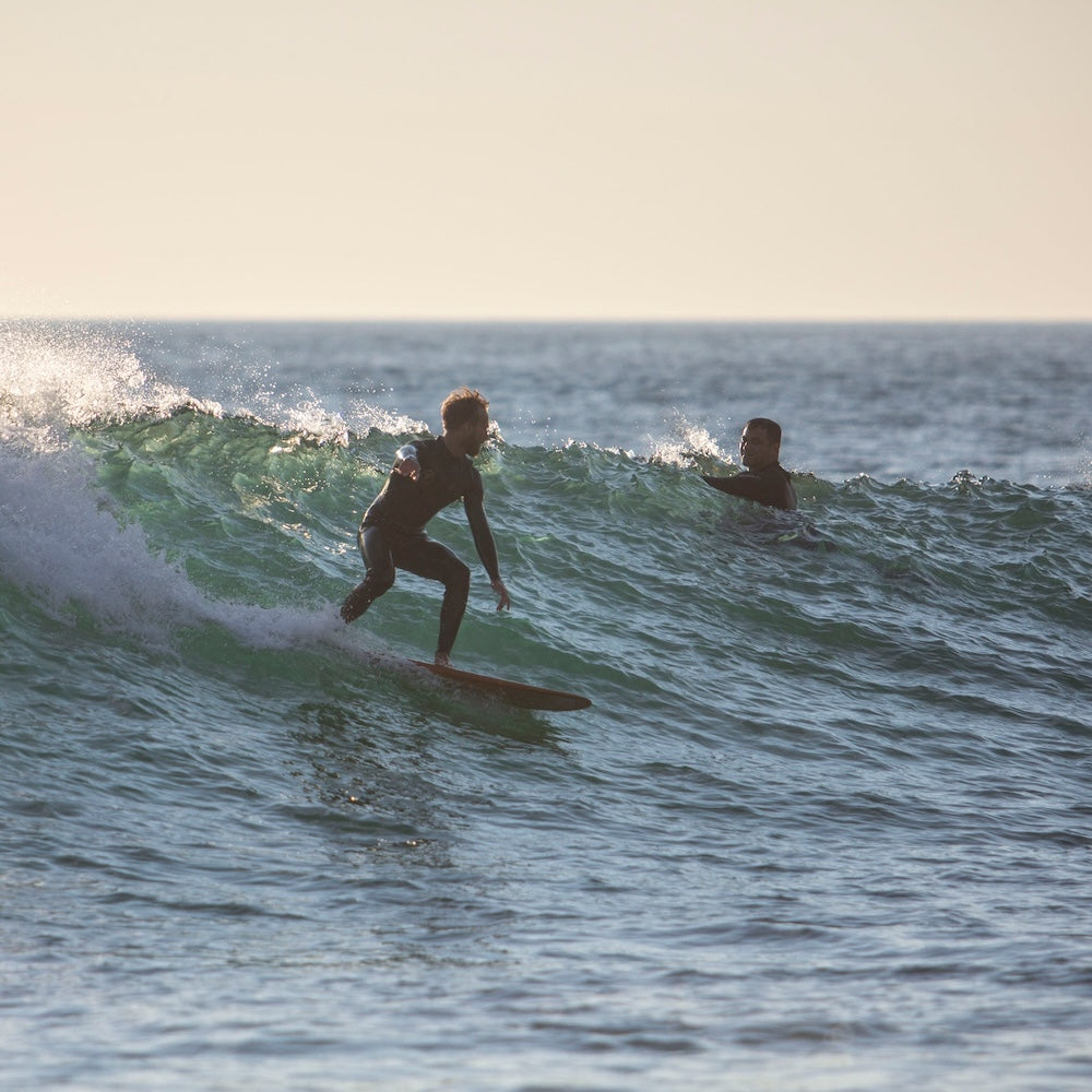 Two surfers in the ocean with one riding a wave and the other waiting.