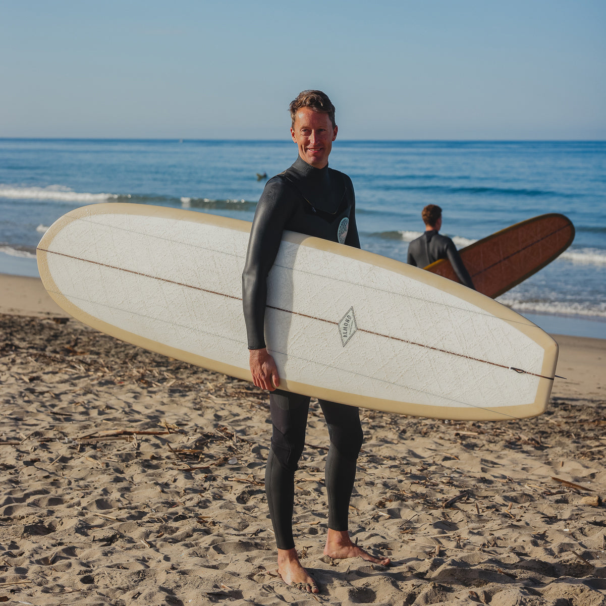 Person holding a surfboard on a beach with another person in the background
