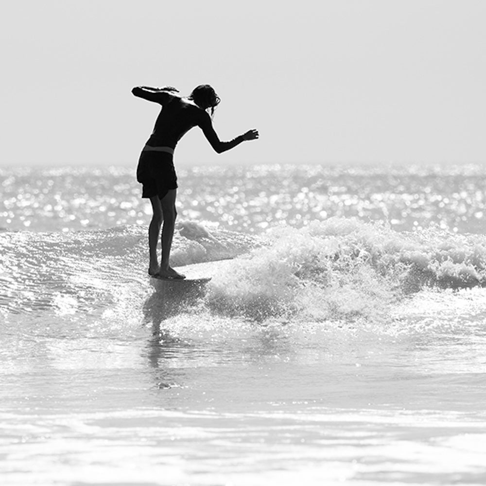 Black and white silhouette of a person surfing on a wave.
