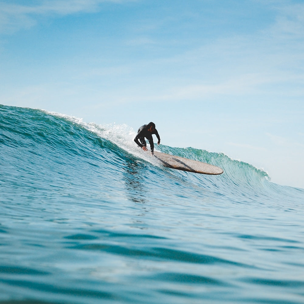 Person surfing on a wave with clear blue sky