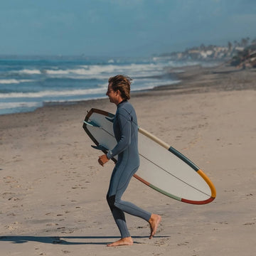 Person in a wetsuit walking on a beach with a surfboard