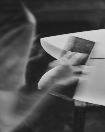 Black and white photo of a person sanding a surfboard