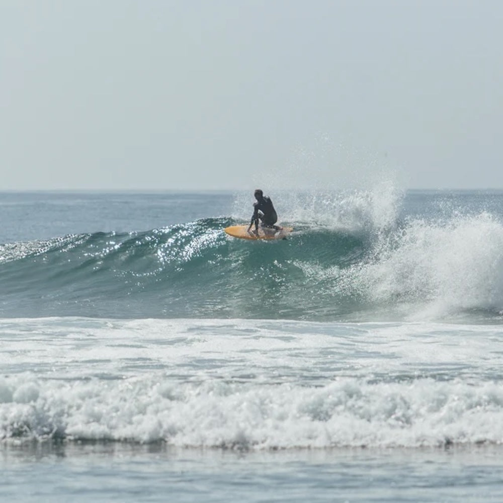 Person surfing on a wave in the ocean with a clear sky.