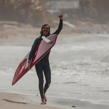 Person in a wetsuit holding a surfboard on a beach