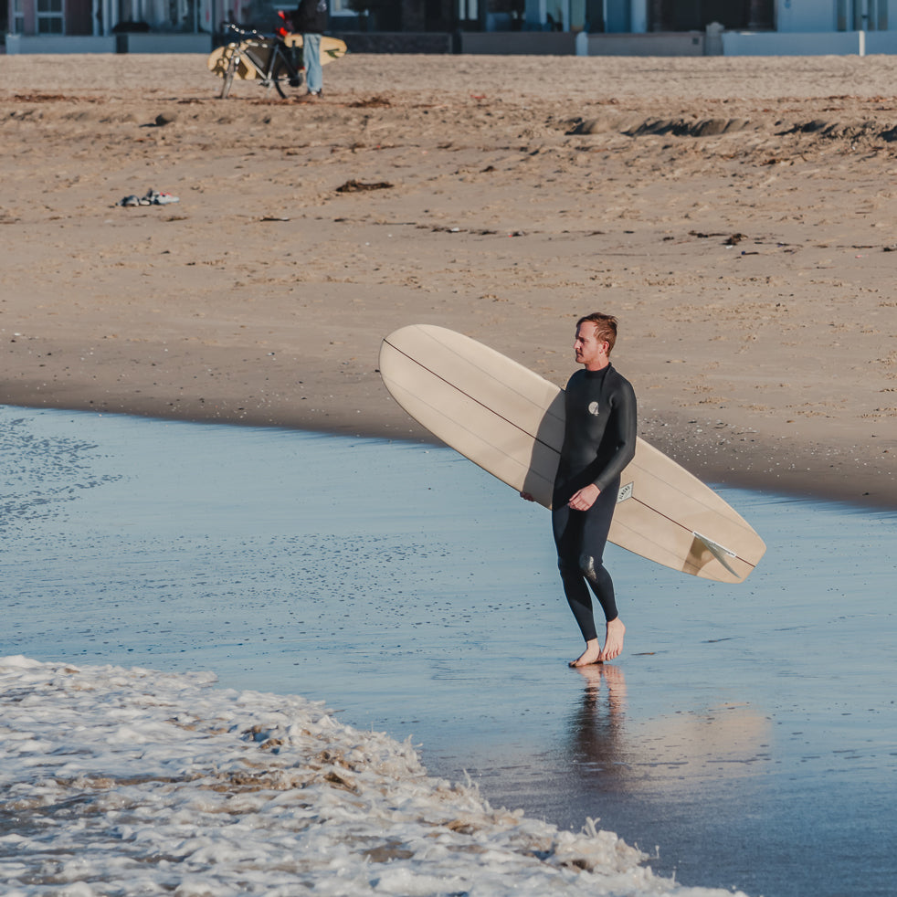 Man in a wetsuit holding a surfboard on a beach